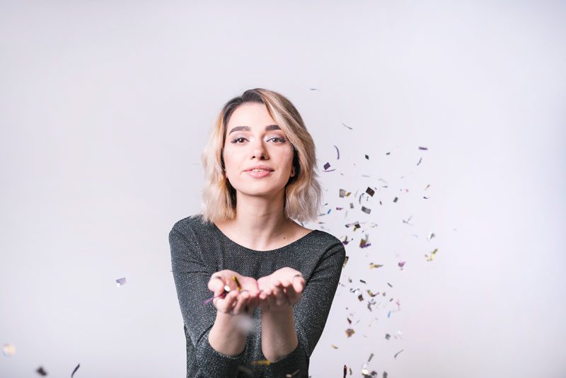 Smiling woman blowing confetti from her hands